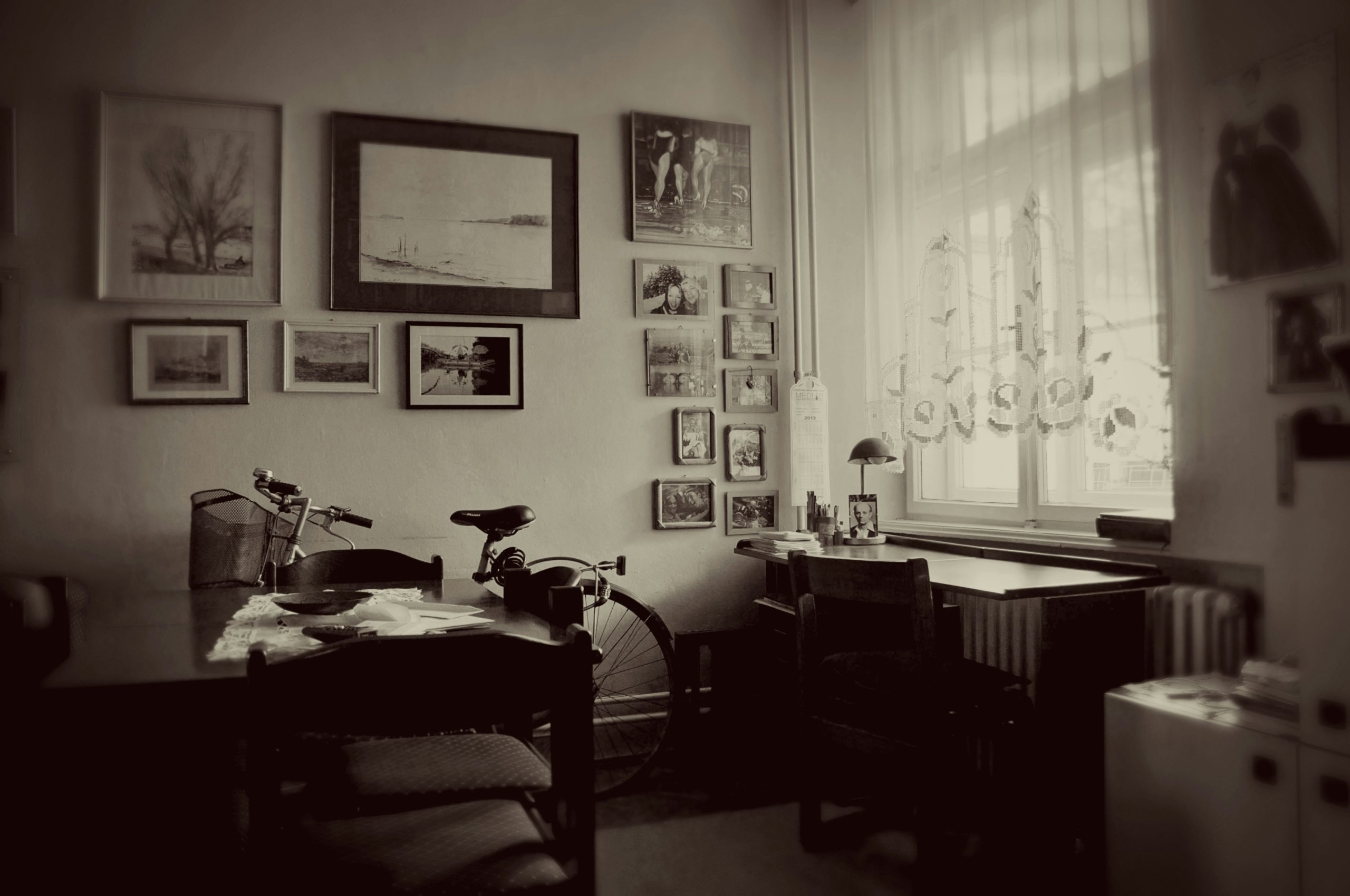 piece en noir et blanc avec deux bureau, des cadres photos accrochés au mur et un velo